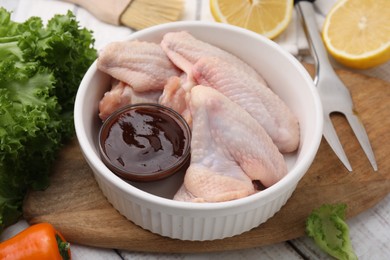 Photo of Fresh marinade, raw chicken wings and other products on rustic wooden table, closeup