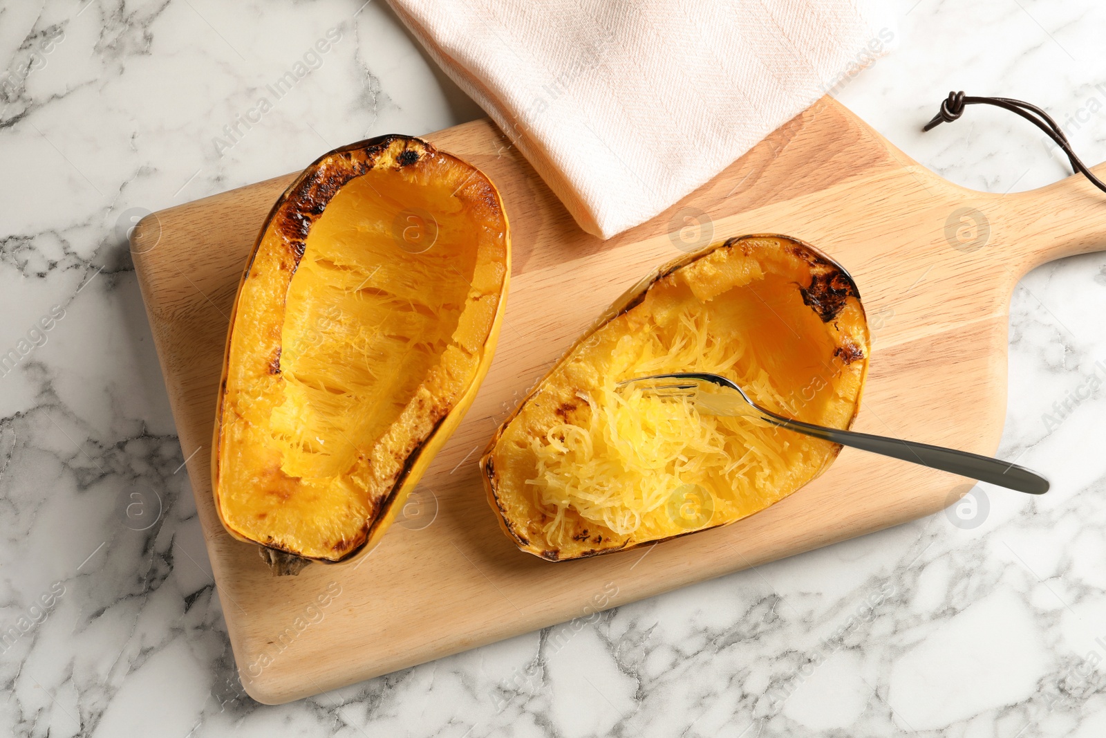 Photo of Wooden board with cooked spaghetti squash and fork on table, top view