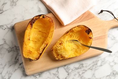 Wooden board with cooked spaghetti squash and fork on table, top view