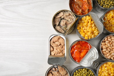 Open tin cans with different vegetables and fish meat on light table, flat lay. Space for text