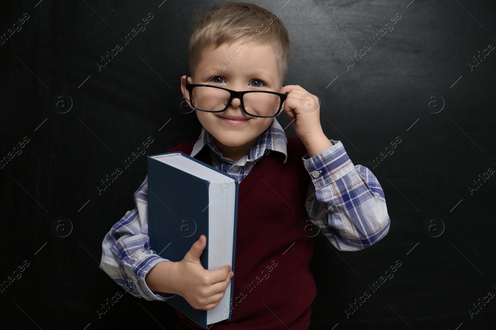 Photo of Cute little child wearing glasses near chalkboard. First time at school