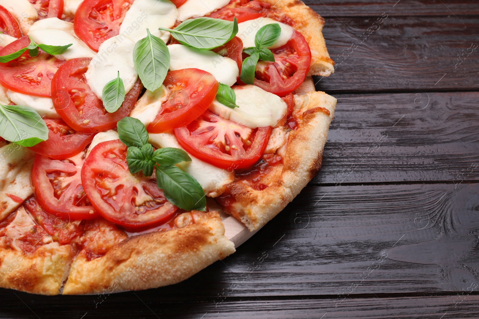 Photo of Delicious Caprese pizza with tomatoes, mozzarella and basil on dark wooden table, closeup. Space for text