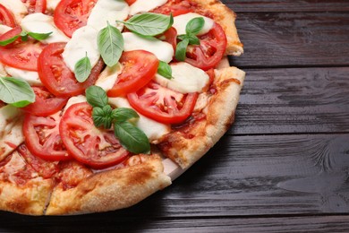 Photo of Delicious Caprese pizza with tomatoes, mozzarella and basil on dark wooden table, closeup. Space for text