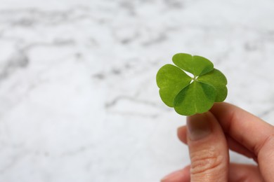 Photo of Woman holding green four leaf clover at white marble table, closeup. Space for text