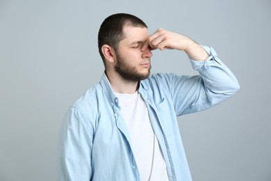 Man suffering from runny nose on light grey background