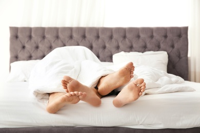 Gay couple cuddling under blanket on bed, closeup of feet