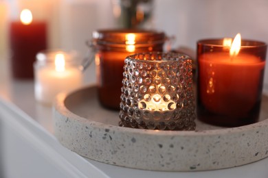 Burning candles on mantel near white wall indoors