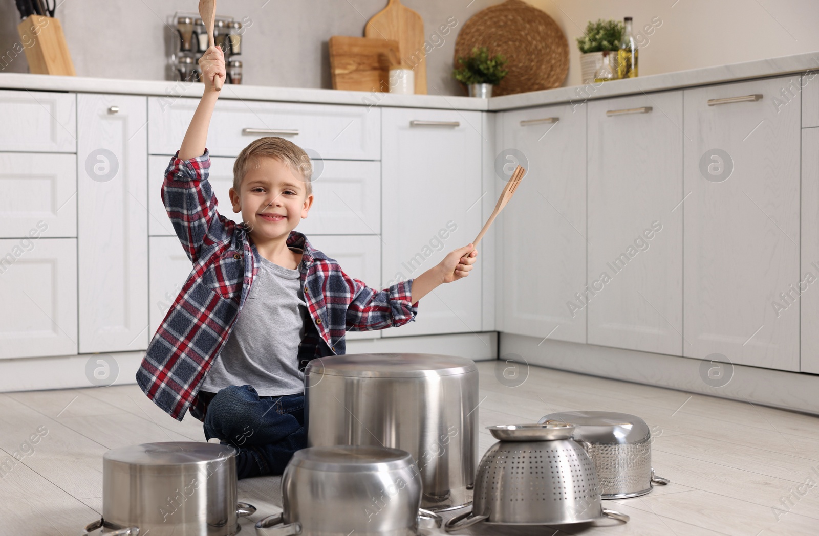 Photo of Little boy pretending to play drums on pots in kitchen