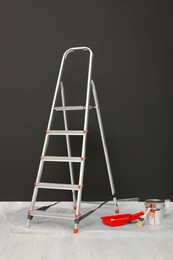 Metallic folding ladder and painting tools near gray wall indoors