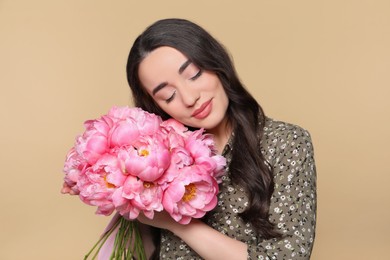 Beautiful young woman with bouquet of pink peonies on light brown background