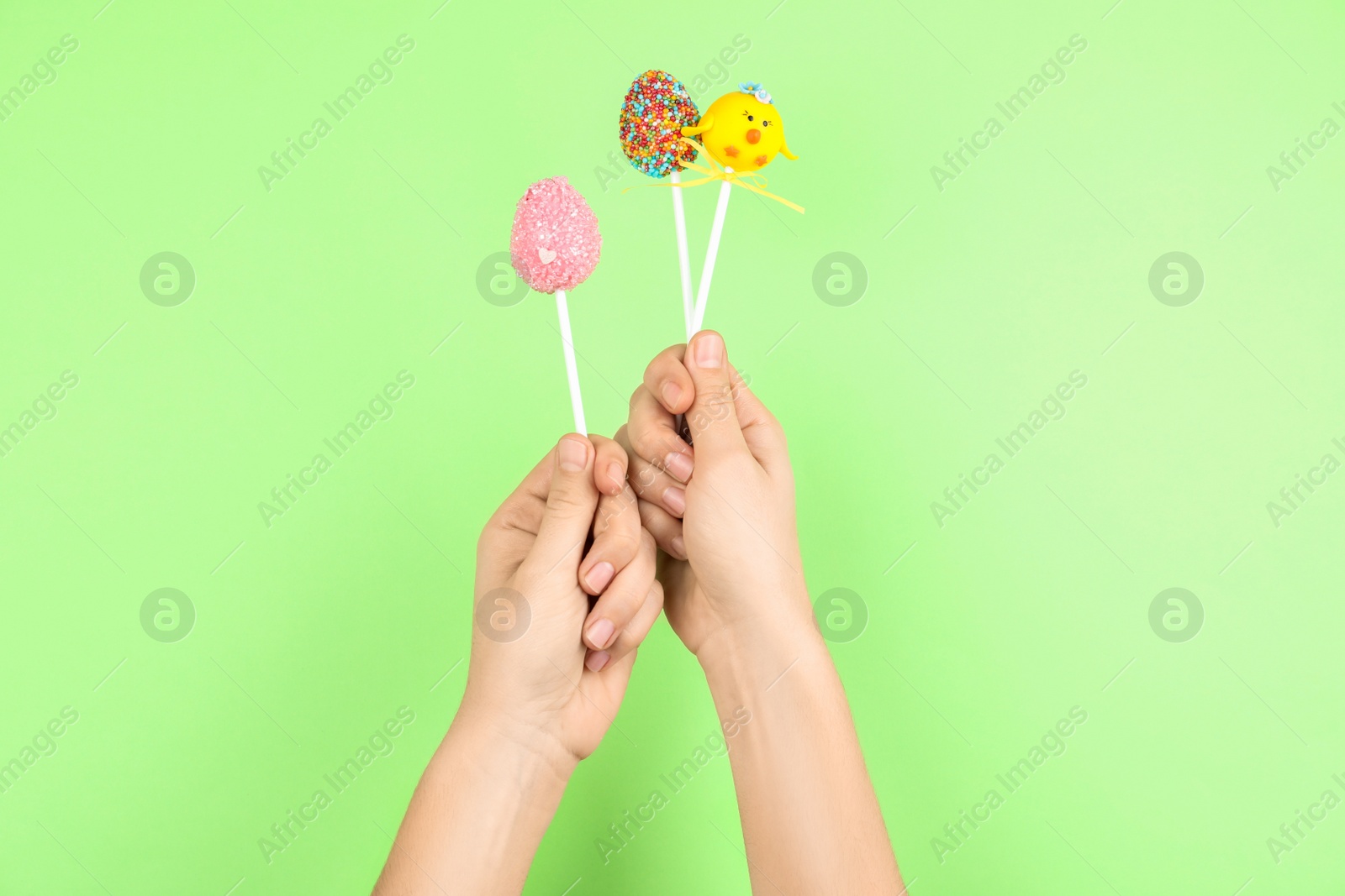 Photo of Woman with delicious cake pops on light green background, closeup. Easter holiday