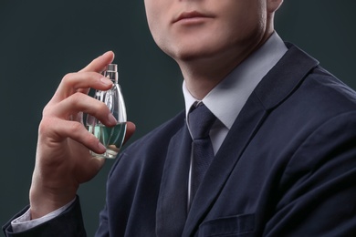 Photo of Handsome man in suit using perfume on dark background, closeup