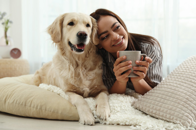 Photo of Young woman with cup of drink and her Golden Retriever at home. Adorable pet