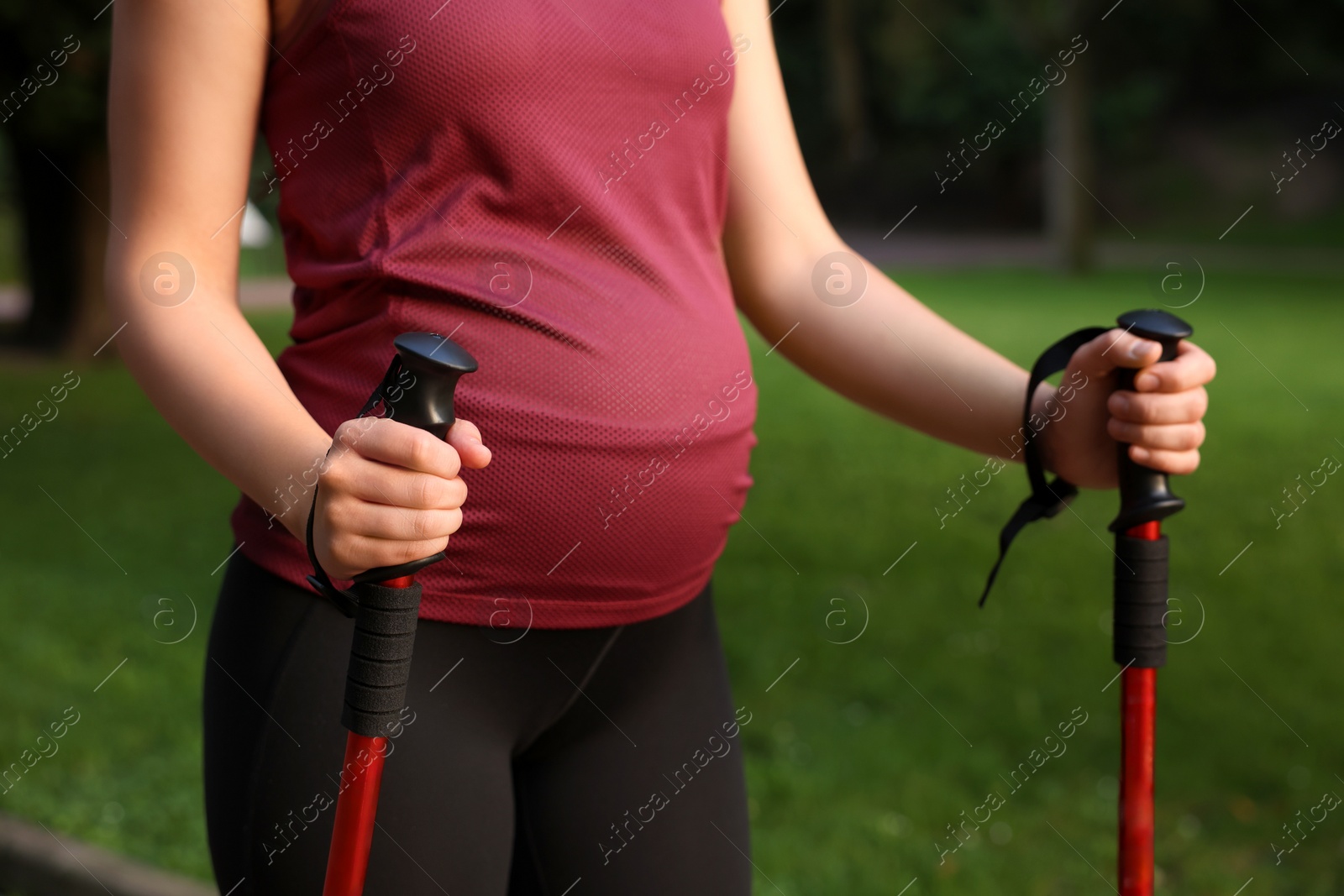 Photo of Pregnant woman practicing Nordic walking with poles outdoors, closeup