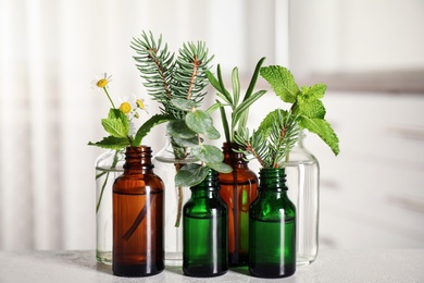 Glass bottles of different essential oils with plants on table