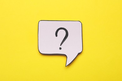 Paper speech bubble with question mark on yellow background, top view