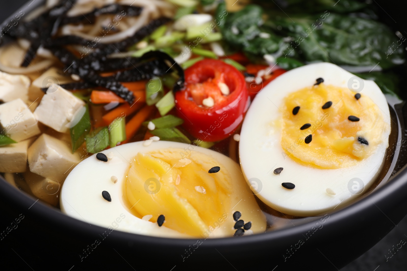 Photo of Delicious vegetarian ramen with egg, tofu and vegetables in bowl, closeup. Noodle soup