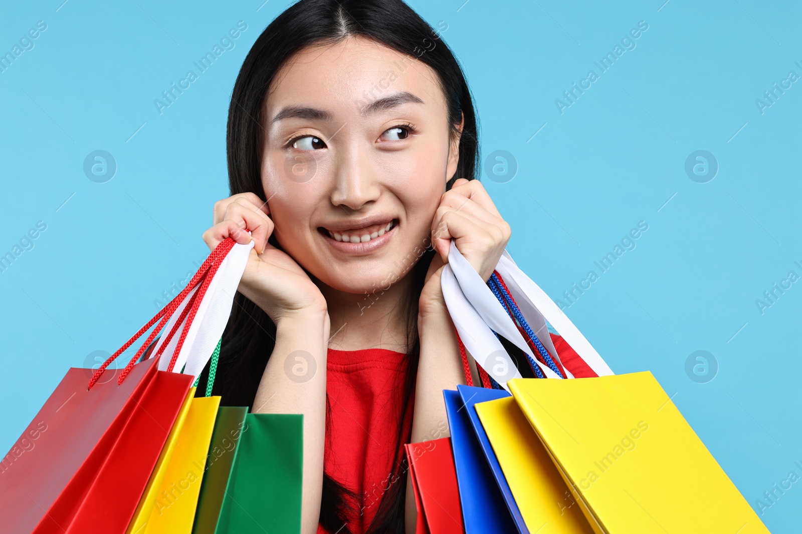 Photo of Happy woman with shopping bags on light blue background