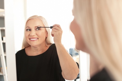 Photo of Mature woman applying makeup near mirror at home