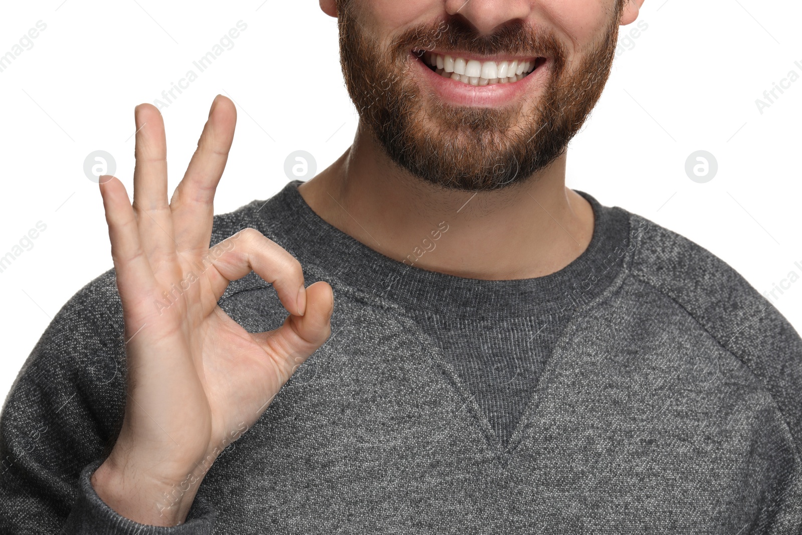 Photo of Smiling man with healthy clean teeth showing ok gesture on white background, closeup