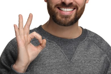 Smiling man with healthy clean teeth showing ok gesture on white background, closeup