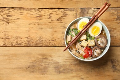 Photo of Bowl of delicious ramen and chopsticks on wooden table, top view with space for text. Noodle soup