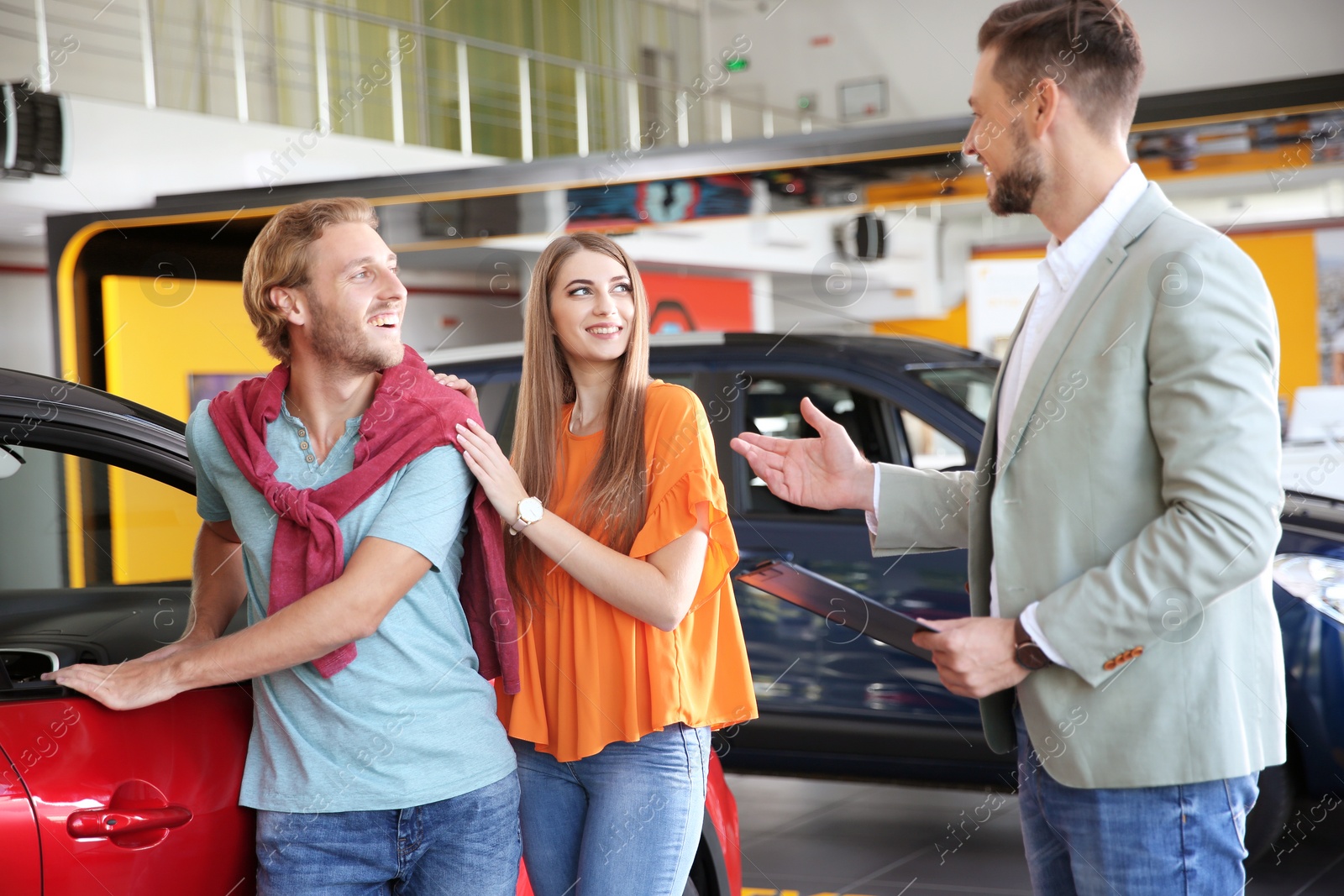 Photo of Salesman with clipboard consulting young couple in modern car dealership