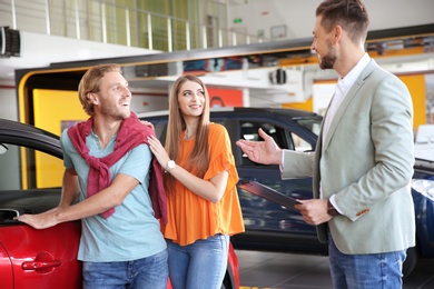 Salesman with clipboard consulting young couple in modern car dealership