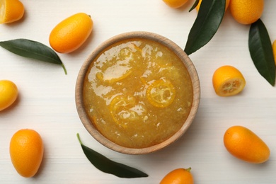 Photo of Delicious kumquat jam in bowl and fresh fruits on white wooden table, flat lay