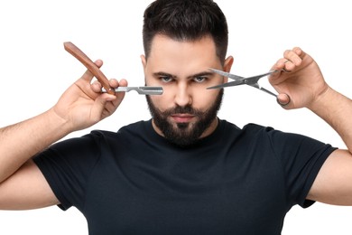 Handsome young man with mustache holding blade and scissors on white background