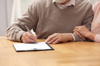 Senior couple signing Last Will and Testament at wooden table, closeup