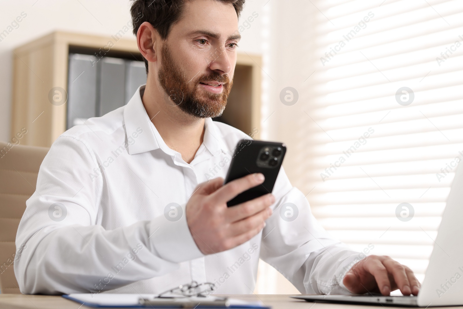 Photo of Man with smartphone using laptop at table in office