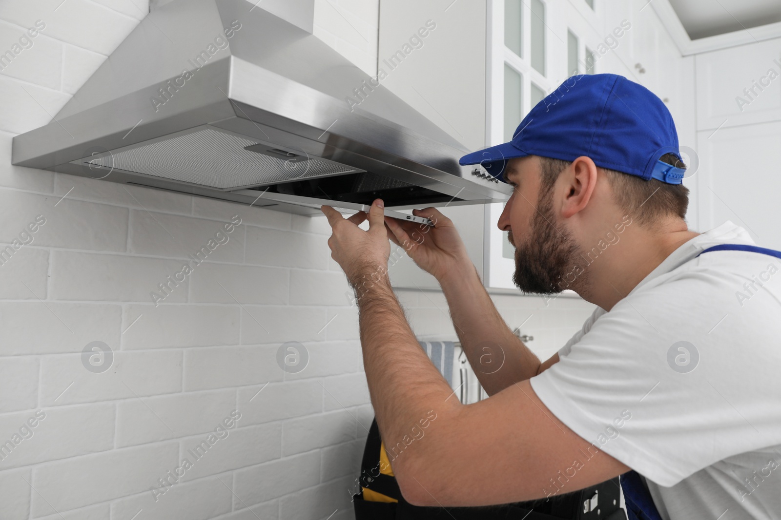 Photo of Worker repairing modern cooker hood in kitchen