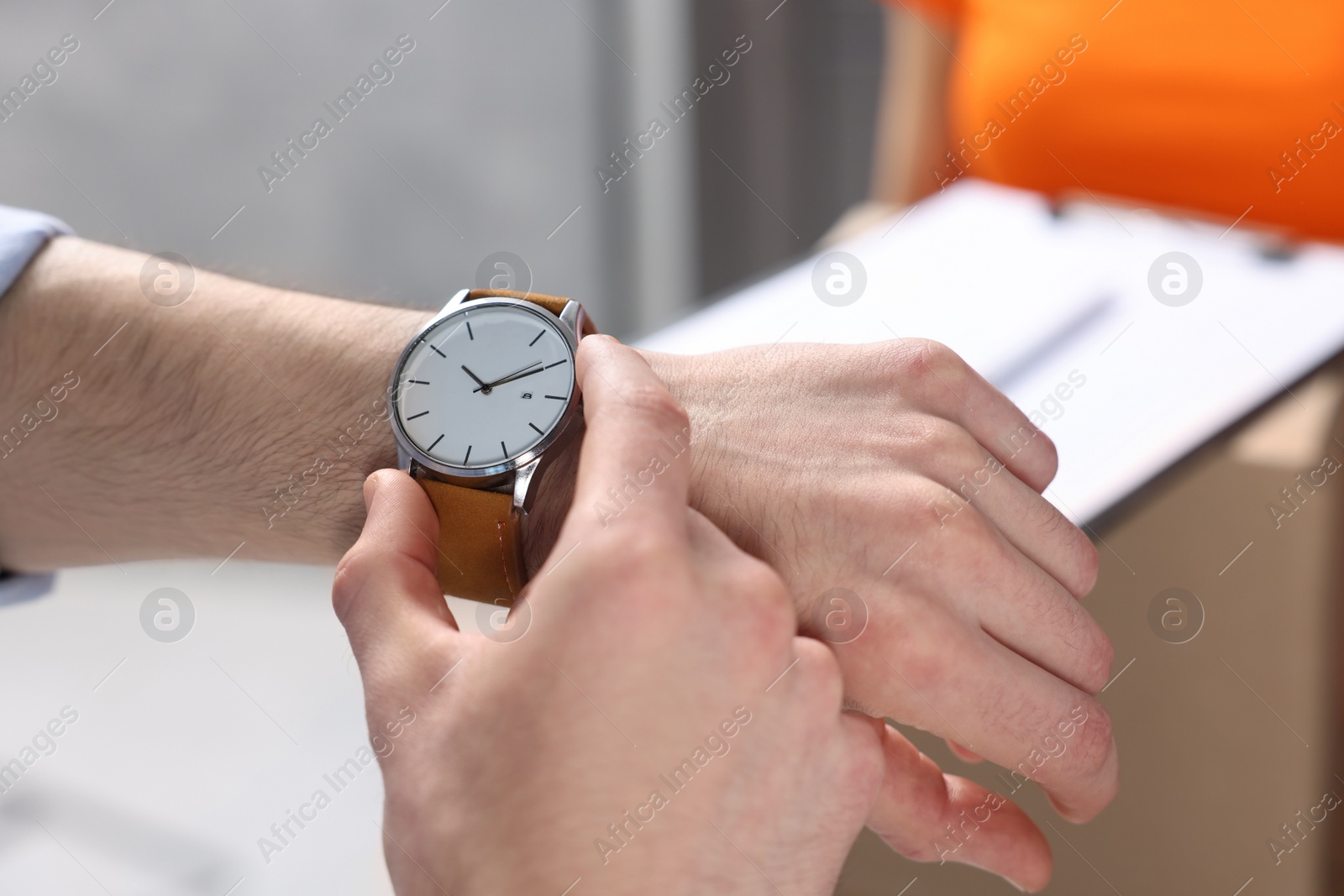 Photo of Closeup view of man checking time near courier with parcels indoors