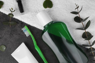 Photo of Fresh mouthwash in bottle, toothbrush, toothpaste and dental floss on dark textured table, flat lay