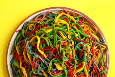 Plate of spaghetti painted with different food colorings on yellow background, top view