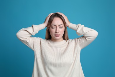 Photo of Young woman suffering from headache on light blue background