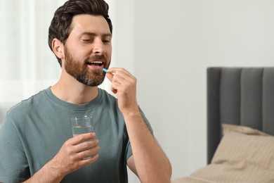 Photo of Handsome man with glass of water taking pill at home, space for text