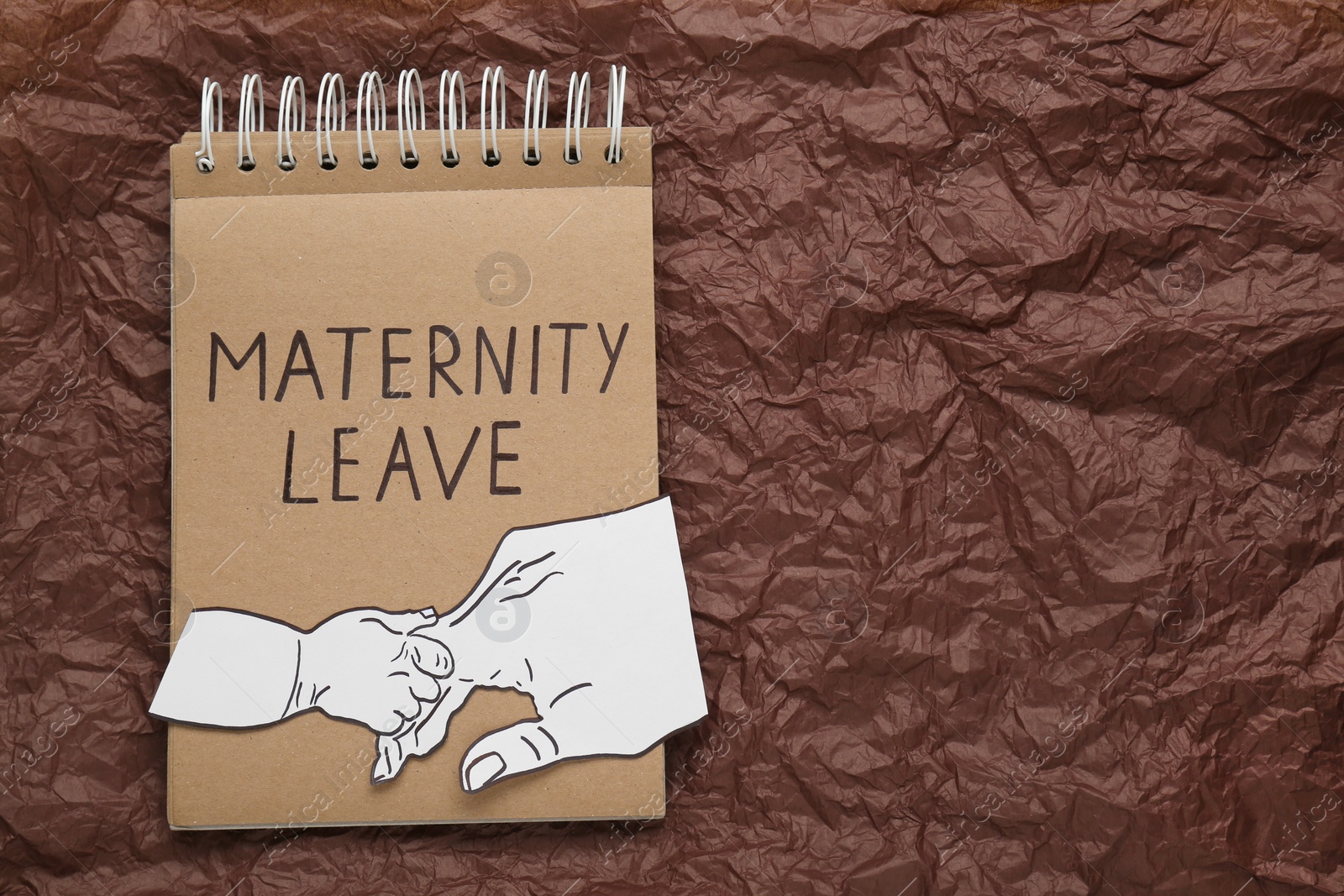 Photo of Notepad with words Maternity Leave and cutout of hands on brown crumpled paper, top view. Space for text
