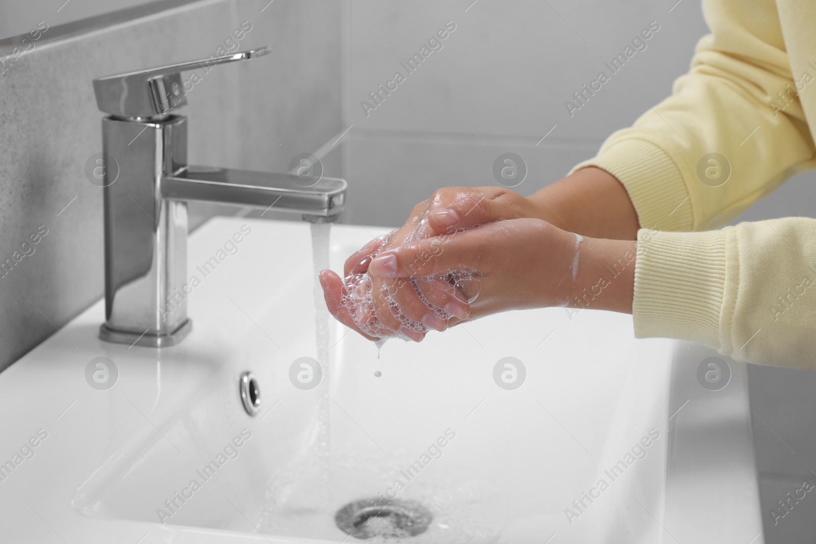 Photo of Woman washing hands with water from tap in bathroom, closeup