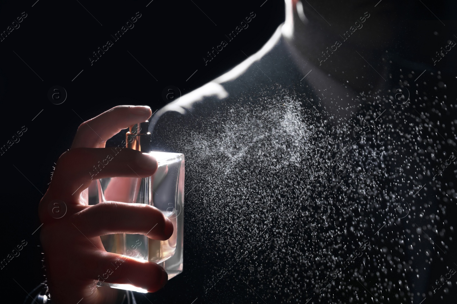 Photo of Man spraying luxury perfume on black background, closeup