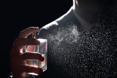 Man spraying luxury perfume on black background, closeup
