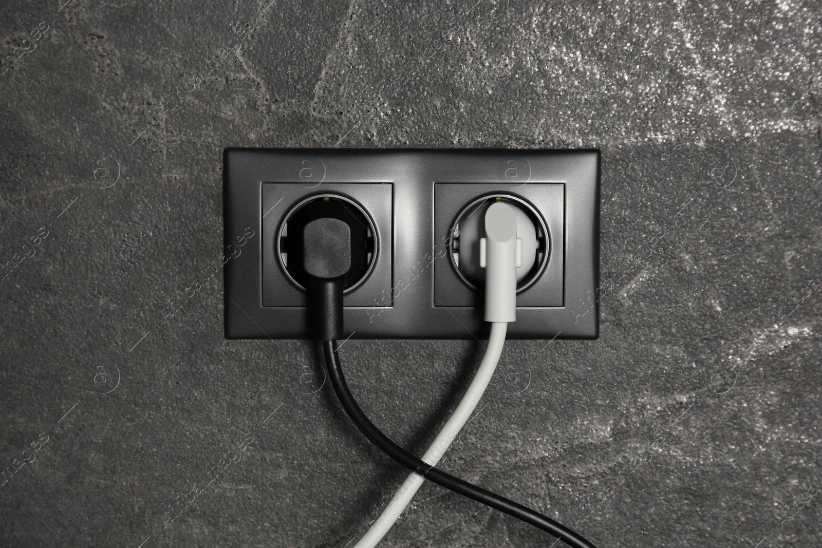 Photo of Power sockets with inserted plugs on dark grey wall. Electrical supply