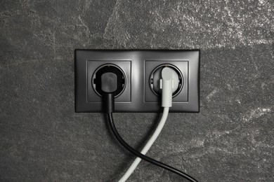 Power sockets with inserted plugs on dark grey wall. Electrical supply