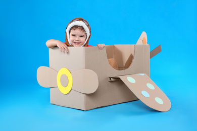 Cute little child playing with cardboard airplane on light blue background