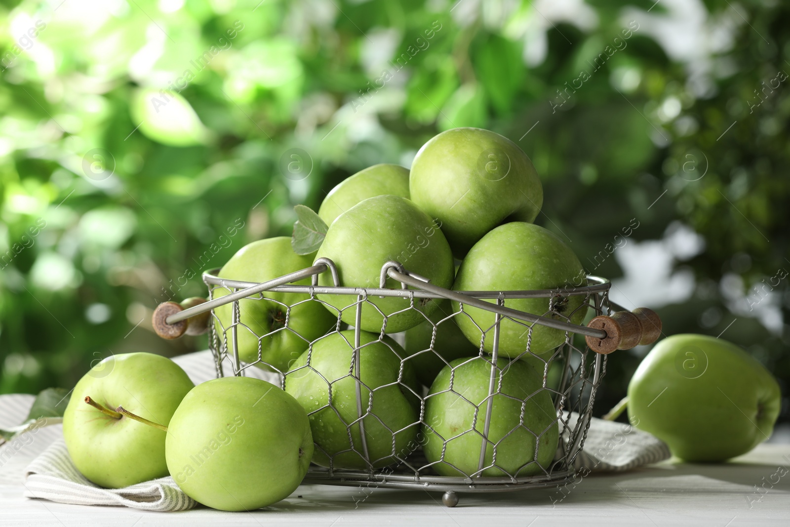Photo of Metal basket with ripe green apples on white table outdoors