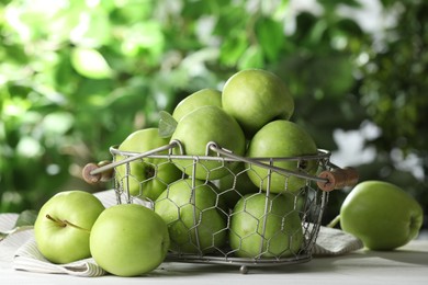 Metal basket with ripe green apples on white table outdoors