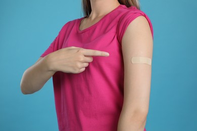 Photo of Vaccinated woman showing medical plaster on her arm against light blue background, closeup