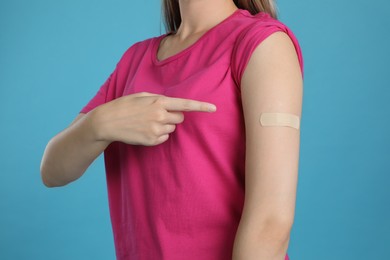 Vaccinated woman showing medical plaster on her arm against light blue background, closeup