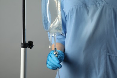 Nurse with IV infusion set on grey background, closeup